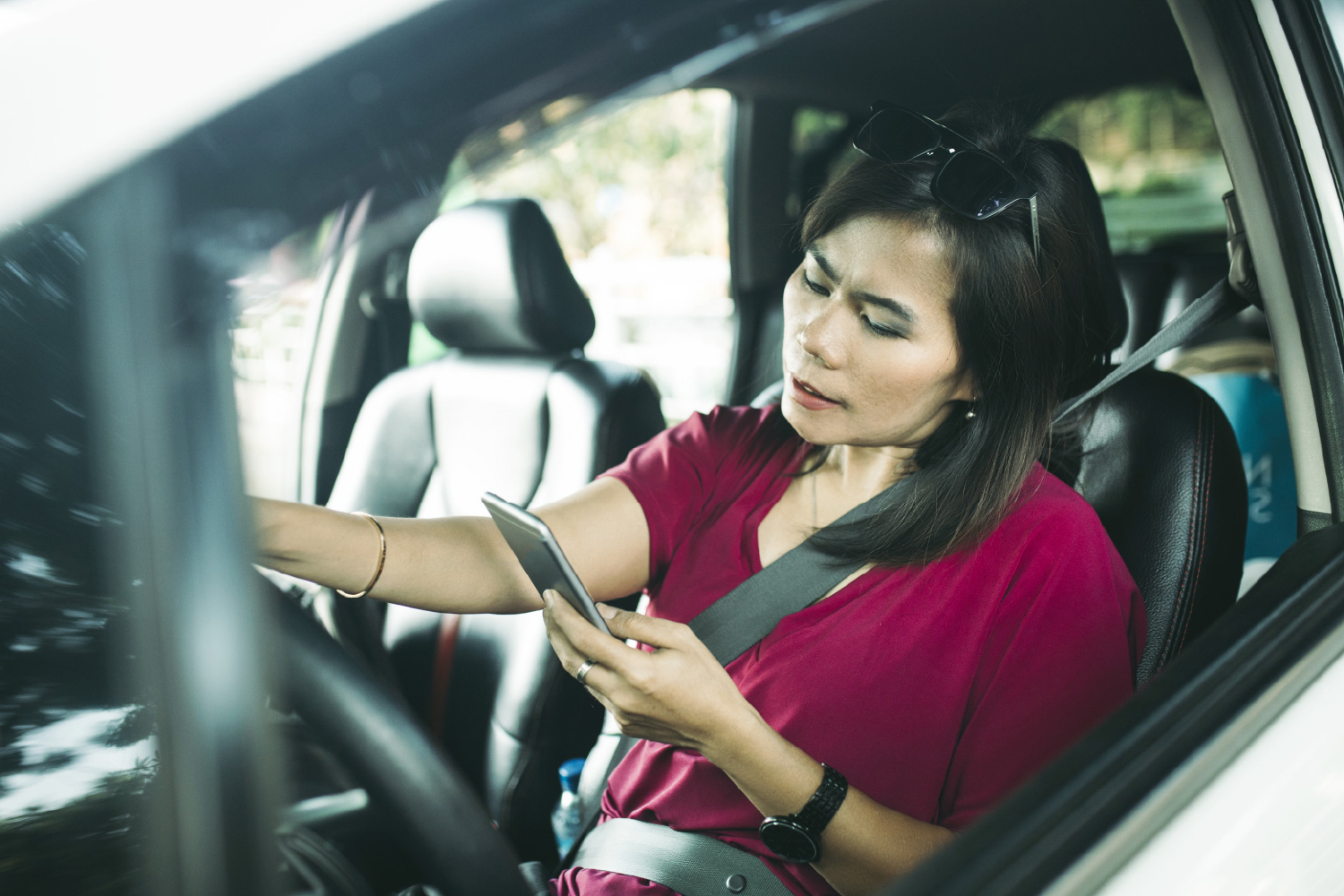 Mujer en auto viendo su celular utilizando la herramienta Consulta SOAT por placa.