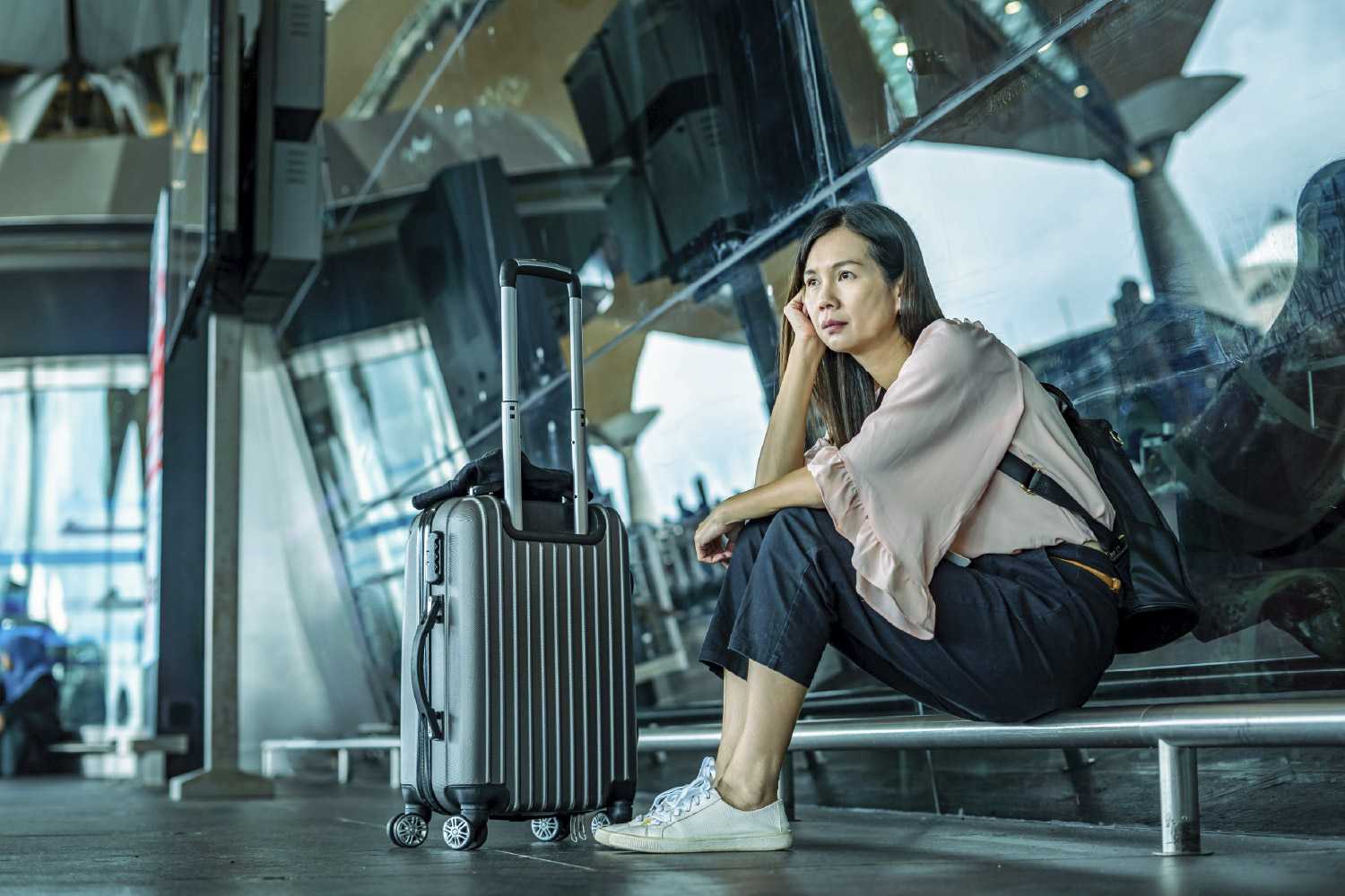 Mujer esperando en el aeropuerto vuelo retrasado cubierto por seguro de viaje